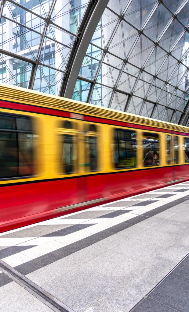 Trem urbano em movimento na plataforma de uma estação com cobertura de vidro